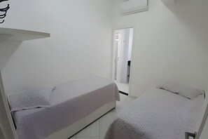 Ein kleines, einfach eingerichtetes Zimmer mit zwei Betten und einem schmalen Flur.