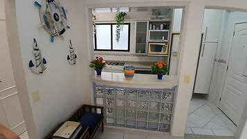 Cocina compacta con refrigerador integrado, una pequeña zona de comedor con banco y elementos decorativos en las paredes.