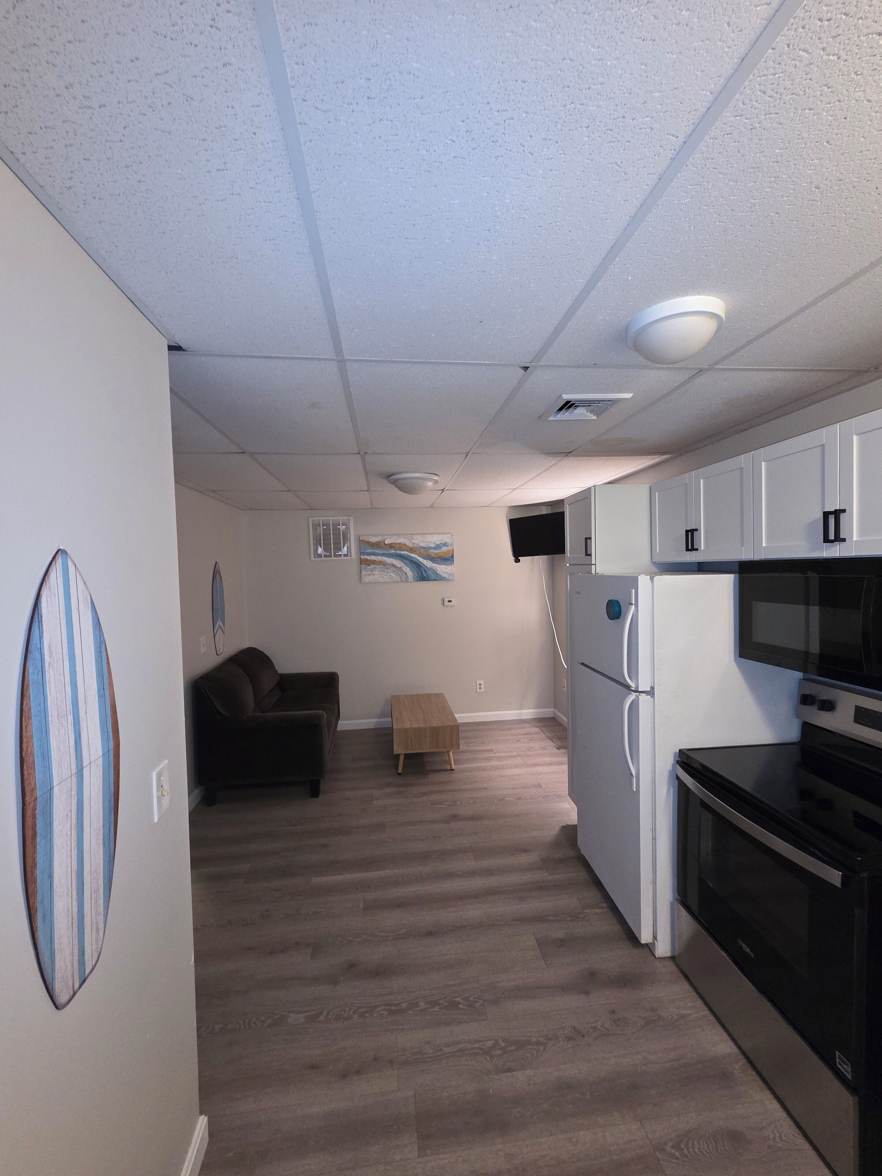 A compact kitchen with a microwave, oven, and refrigerator. There is a small wooden table and a couch in the adjacent living area.