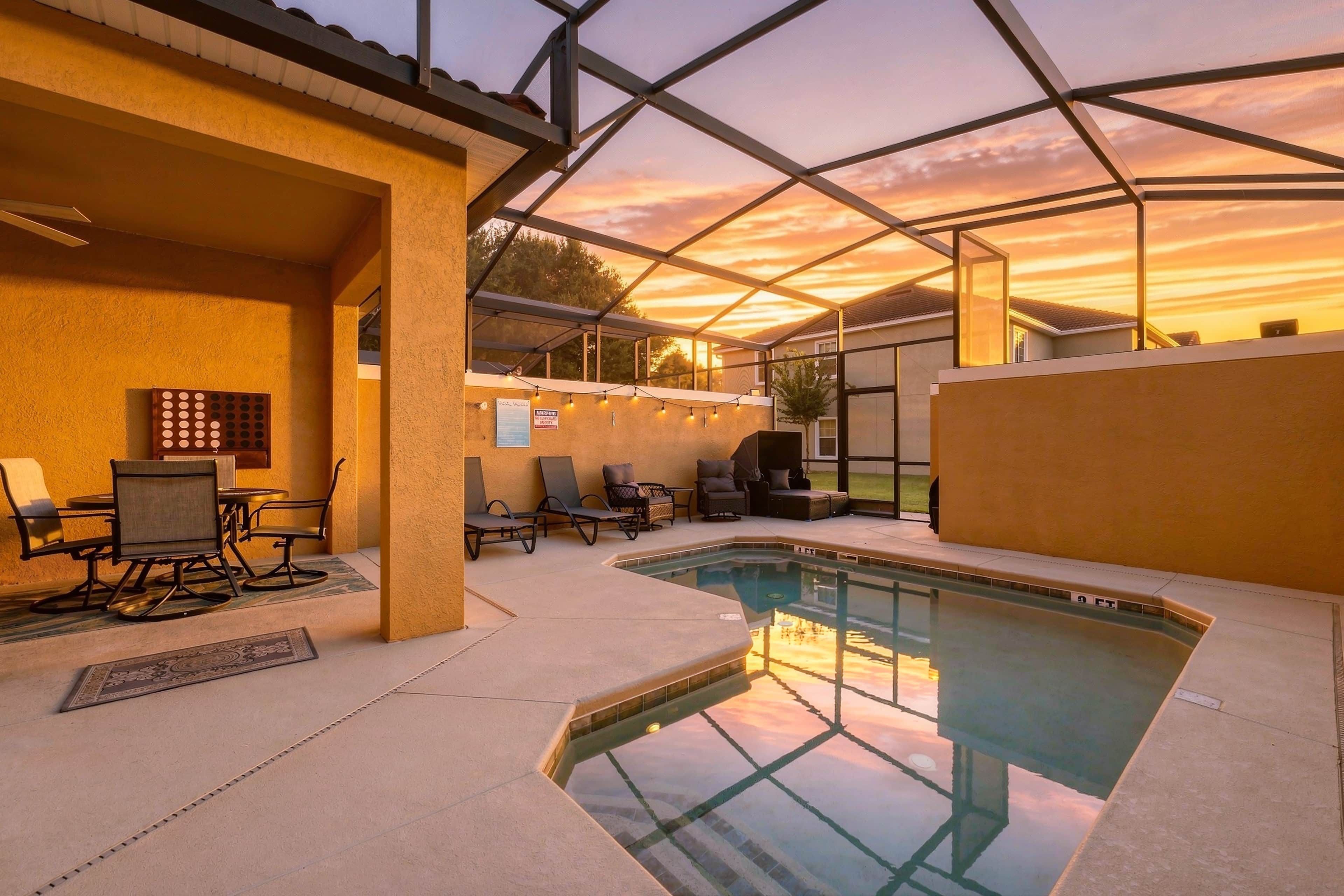 An outdoor pool area with a glass enclosure, lounge chairs, and a dining table.