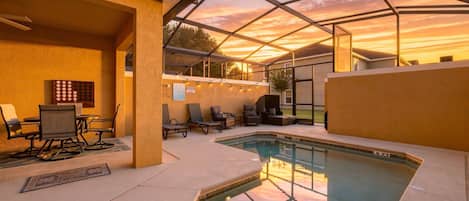 An outdoor pool area with a glass enclosure, lounge chairs, and a dining table.