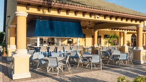 An outdoor cafe with tables and chairs, a covered seating area, and a building with columns and a tiled roof. - Free Pool Heat | Hypoallergenic Private Villa | Lux Resort (Four Corners)