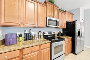 A kitchen with wooden cabinets, a stainless steel microwave, a black refrigerator, a stove, and a purple appliance on the counter. - Free Pool Heat | Hypoallergenic Private Villa | Lux Resort (Four Corners)