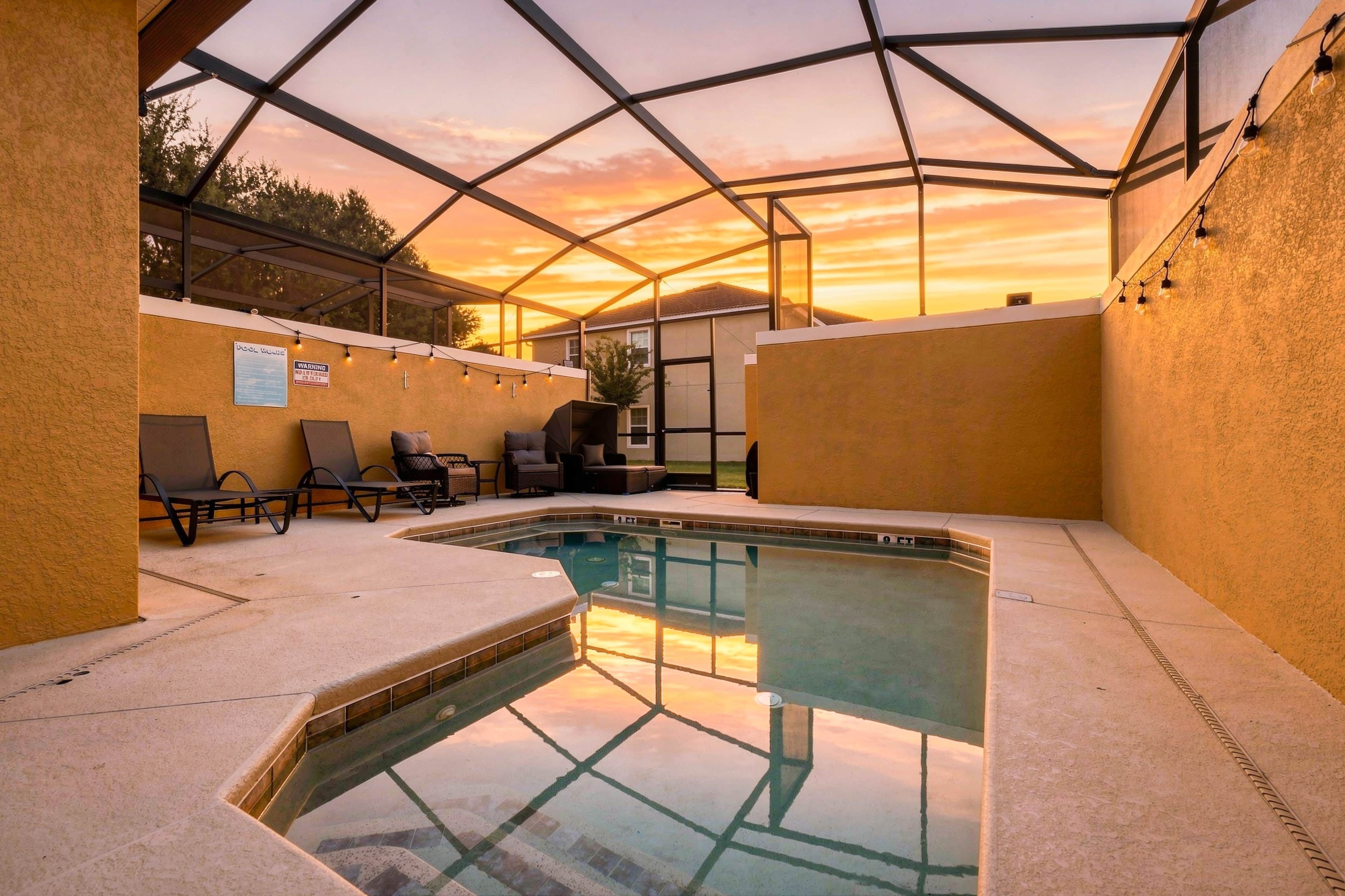 A swimming pool with a glass enclosure, surrounded by lounge chairs and a covered patio area.