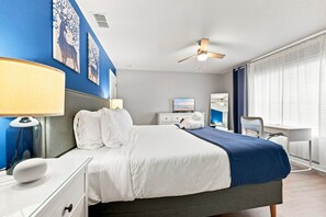 Una habitació d'hotel amb un llit, una taula de treball, una cadira, una làmpada i obra d'art a les parets.