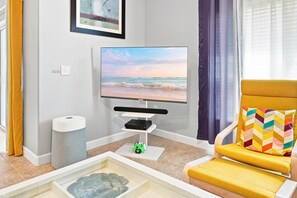 A living room with a flat-screen TV, a gaming console, and a colorful chair. - Free Pool Heat | Hypoallergenic Private Villa | Lux Resort (Four Corners)