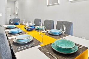 Une table à manger dressée avec des assiettes bleues et vertes, des verres à vin et des couverts, agrémentée d’un chemin de table jaune.