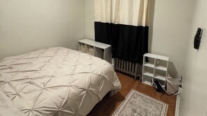 Een slaapkamer met een bed, een plafondventilator, een radiator, een klein wit plankje en een vloerkleed.