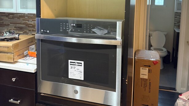 Een keuken met een ingebouwde oven en magnetron, donkere kastjes en een raam.