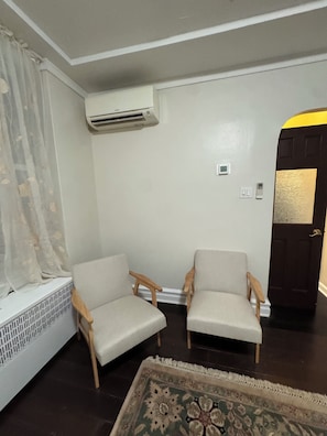 Ein Zimmer mit zwei Holzstühlen, einem Heizkörper, einer Tür mit goldener Verzierung und einem gemusterten Teppich.