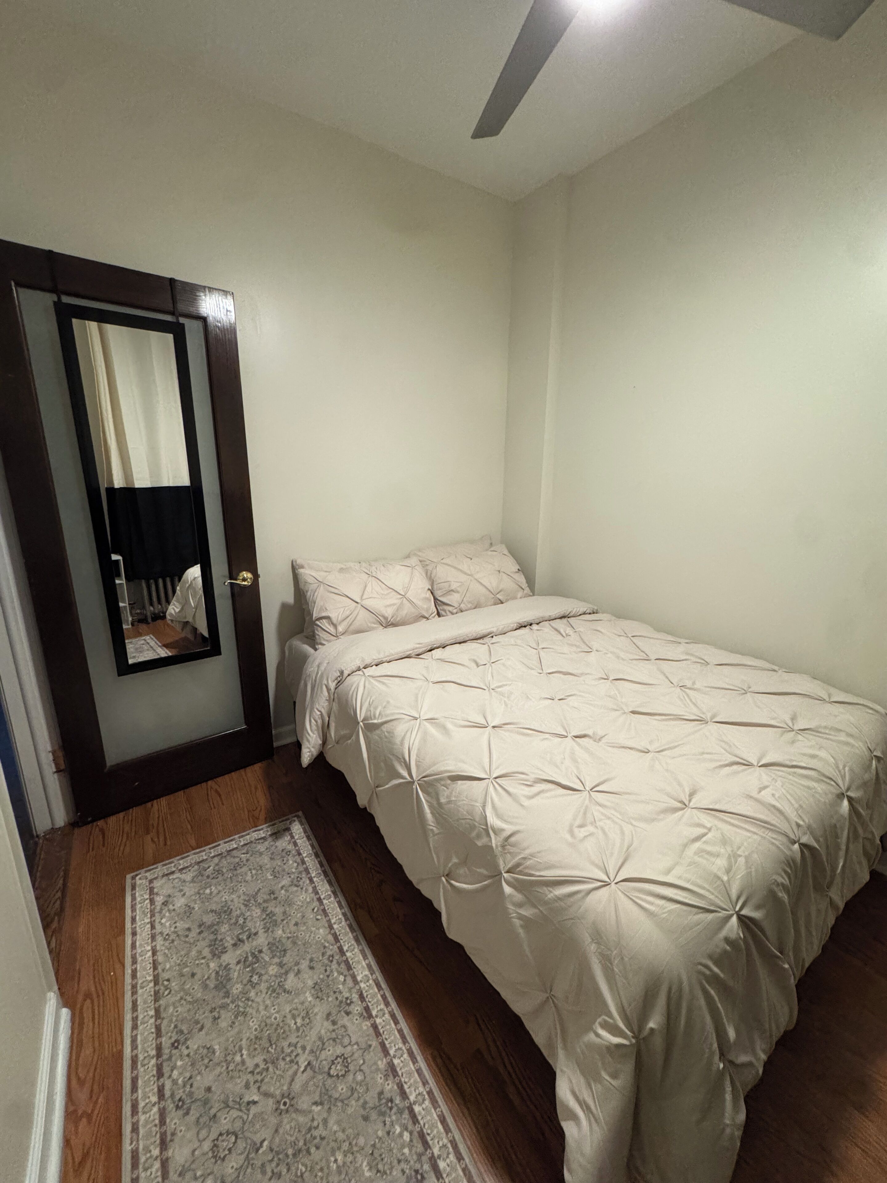 A bedroom with a bed, a rug, and a door with a mirror.