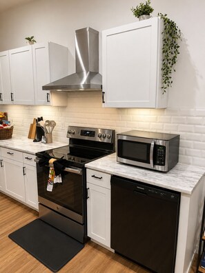 A modern kitchen with white cabinets, stainless steel appliances, and a black oven. - 3BR House Near Mercedes Stadium Sleeps 8 w/ free Parking, A/C, Laundry, & Gazebo (Atlanta)