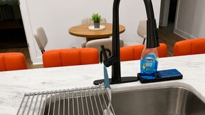 A kitchen with a stainless steel sink, a dish soap bottle, and a metal drying rack. - 3BR House Near Mercedes Stadium Sleeps 8 w/ free Parking, A/C, Laundry, & Gazebo (Atlanta)