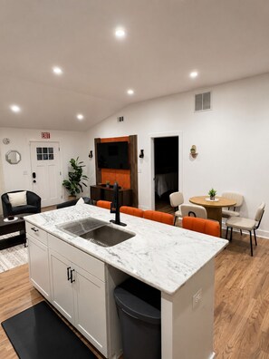 A modern kitchen with a marble countertop, integrated sink, and a dining area with a round table and orange chairs. - 3BR House Near Mercedes Stadium Sleeps 8 w/ free Parking, A/C, Laundry, & Gazebo (Atlanta)