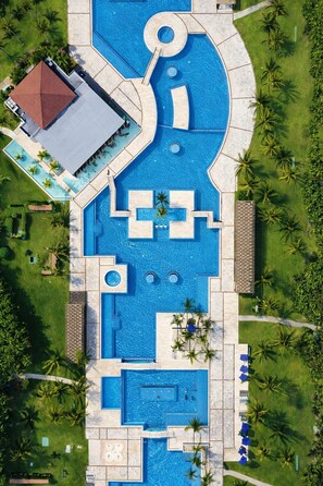 An aerial view of a resort with multiple swimming pools, palm trees, and a covered area. - Luxury Ocean View Penthouse + Resort Pool (Playa del Carmen)