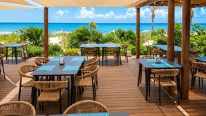 An outdoor dining area with tables and chairs, overlooking a beach with the ocean in the background. - Luxury Ocean View Penthouse + Resort Pool (Playa del Carmen)