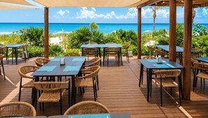 An outdoor dining area with tables and chairs, overlooking a beach with the ocean in the background. - Luxury Ocean View Penthouse + Resort Pool (Playa del Carmen)