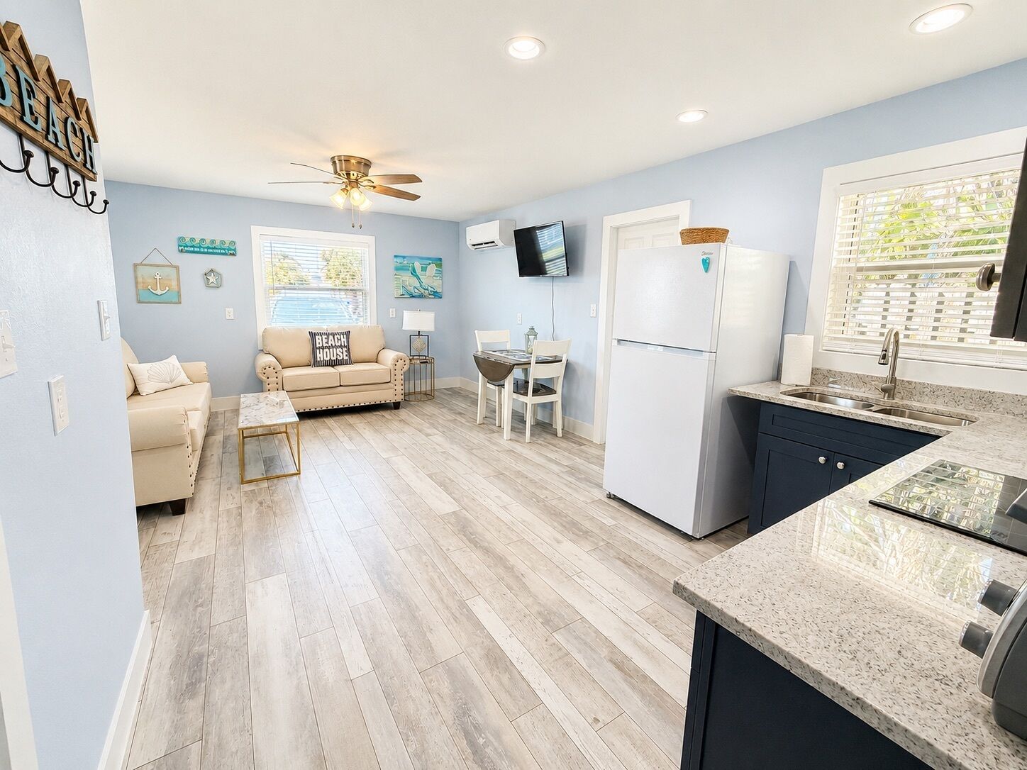 A compact living space with a kitchenette, a ceiling fan, a TV, and a sofa with a beach-themed pillow.