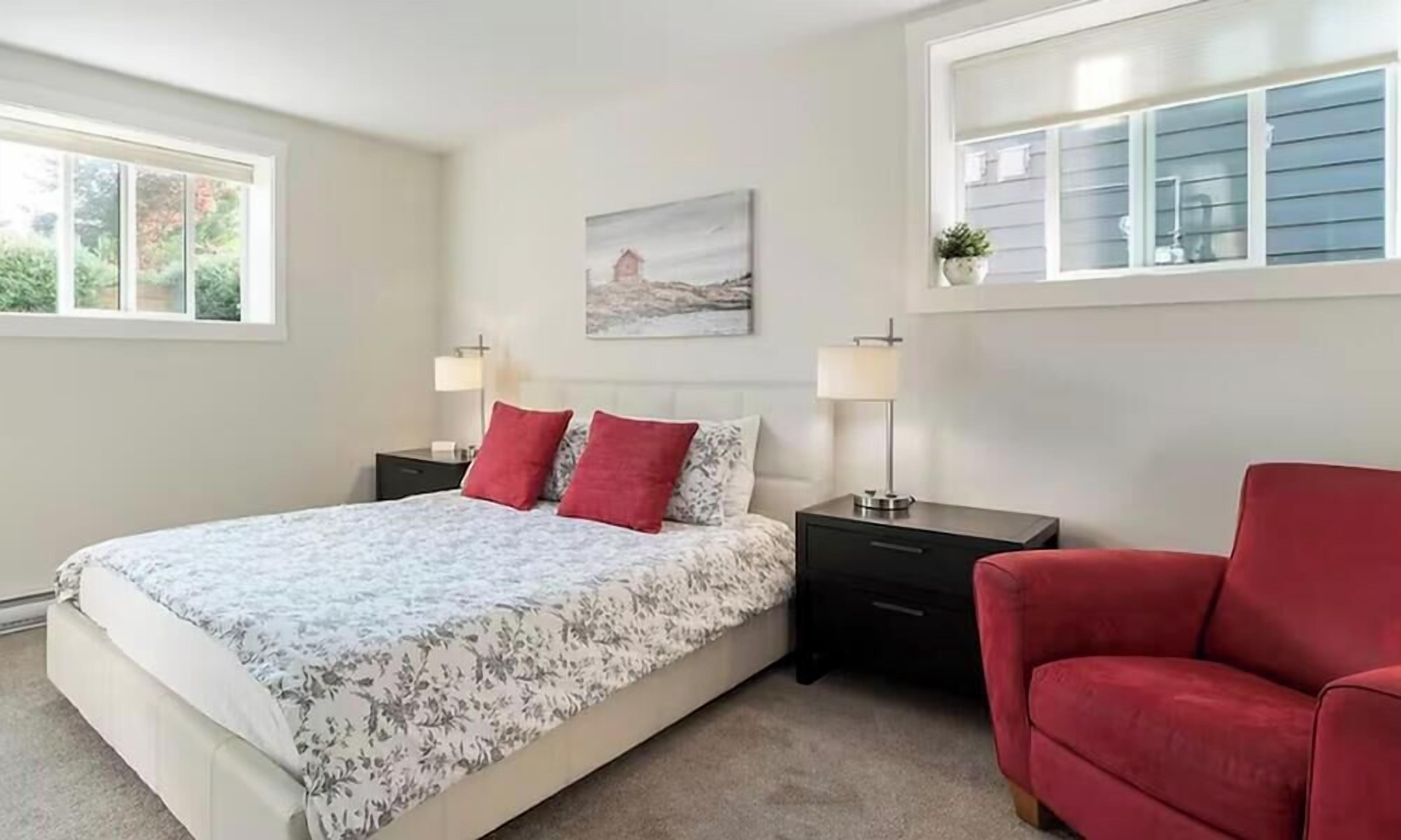 A bedroom with a bed, bedside tables, a red chair, and a window with blinds.