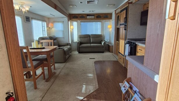 A compact RV interior with a kitchenette, seating area, and a ceiling fan.