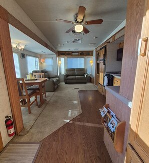 A compact RV interior with a kitchenette, seating area, and a ceiling fan.