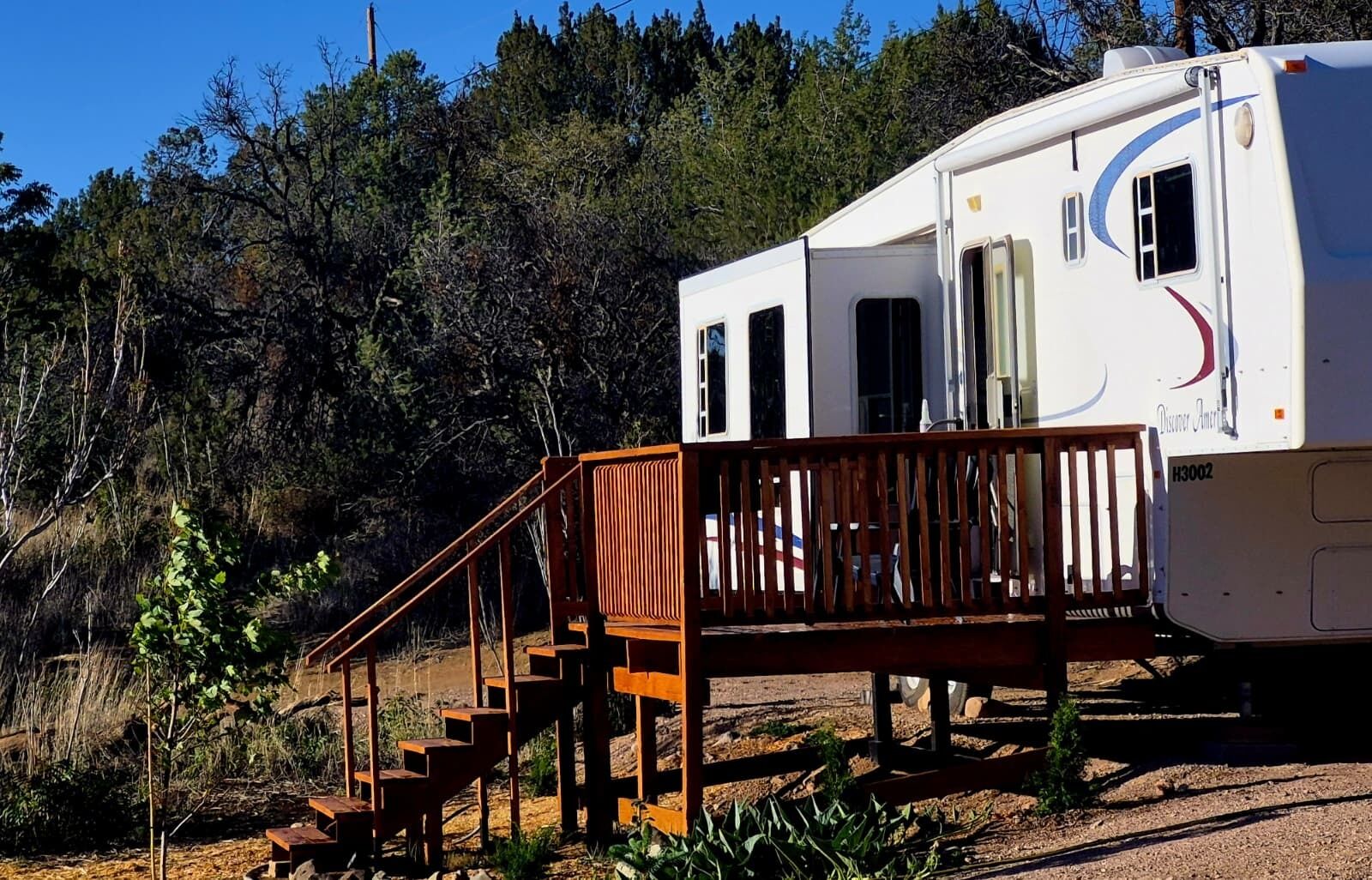 A recreational vehicle with a wooden deck and stairs leading to a covered area.
