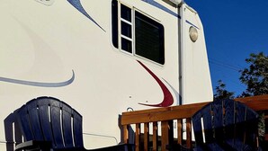 A recreational vehicle with a deck, two Adirondack chairs, and a wooden railing.