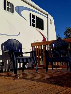 A recreational vehicle with a deck, two Adirondack chairs, and a wooden railing. - Cozy One Bedroom Glamping Camper (Silver City)