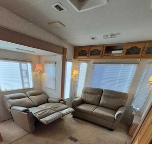 Interior de una caravana compacta con dos sofás reclinables, armarios superiores y lámparas integradas.