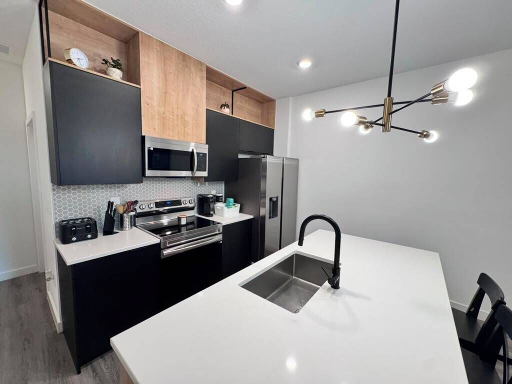 Uma cozinha moderna com uma ilha central, eletrodomésticos embutidos e luminária pendente.