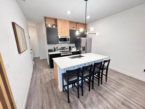 A modern kitchen with a central island, black bar stools, and a pendant light.