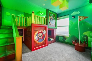 Ein Spielzimmer mit einem Mario-Bettenmotiv, einer Treppe und grünen Wänden.