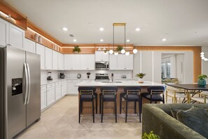 A modern kitchen with a central island, bar stools, a refrigerator, and a dining area with a table and chairs. - 10 BD/ 8 BA/ Windsor Cay (1007 CR) (Clermont)