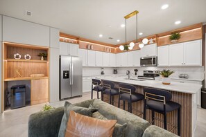 Una cocina moderna con armarios blancos, electrodomésticos de acero inoxidable y una isla central con taburetes de bar.