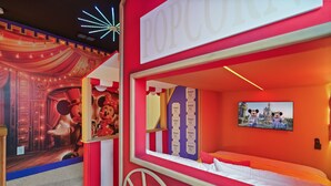 Um quarto temático com parede listrada em vermelho e branco, uma cama, uma TV fixada na parede e um cartaz do Mickey Mouse.