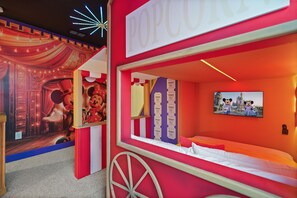 Ein thematisch gestaltetes Zimmer mit einer rot-weiß gestreiften Wand, einem Bett, einem wandmontierten Fernseher und einem Mickey Mouse-Poster.