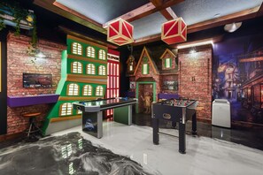 Ein Zimmer mit einem Kicker, einem Fernsehbildschirm und einer Ziegelwand mit roter und grüner Fassade.