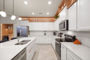 A modern kitchen with white cabinetry, stainless steel appliances, and a central island with a sink. - 10 BD/ 8 BA/ Windsor Cay (1007 CR) (Clermont)