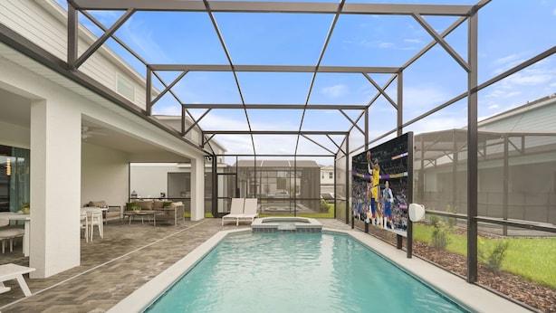 Piscina com área de varanda coberta, mobiliário de exterior e uma grande tela exibindo um evento esportivo.