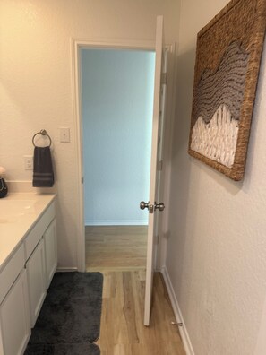 A bathroom with a white sink, a towel ring, a dark rug, and a door leading to a room with a light blue wall and wooden flooring. - Charming/ Modern  4-bedroom townhome in San Antonio (San Antonio)