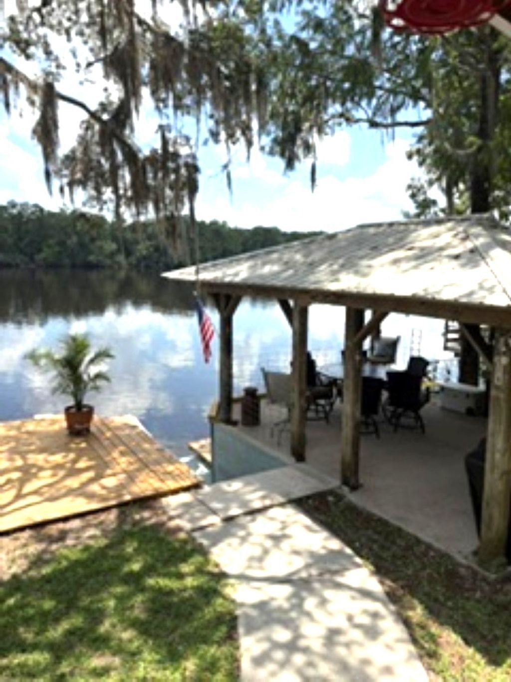 A covered outdoor seating area with a view of a lake, a flag, and a potted plant.
