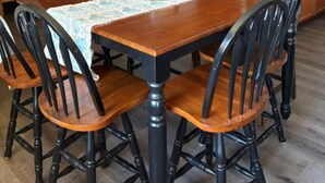 Un coin repas avec une table et des chaises en bois, un buffet blanc et un espace cuisine doté de meubles en bois et d’un évier.