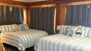 Une chambre avec deux lits, des murs en bois, un ventilateur de plafond et une fenêtre avec des rideaux.