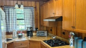 Une cuisine avec des meubles de rangement en bois, une cuisinière, un évier et une fenêtre agrémentée de rideaux à carreaux.