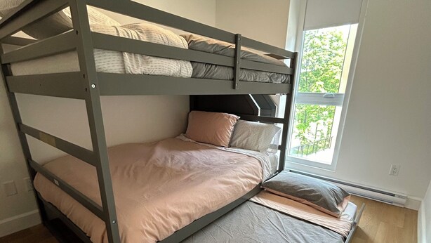 Ein Etagenbett mit Holzrahmen und grauer Bettwäsche in einem Zimmer mit Holzboden und einem großen Fenster.
