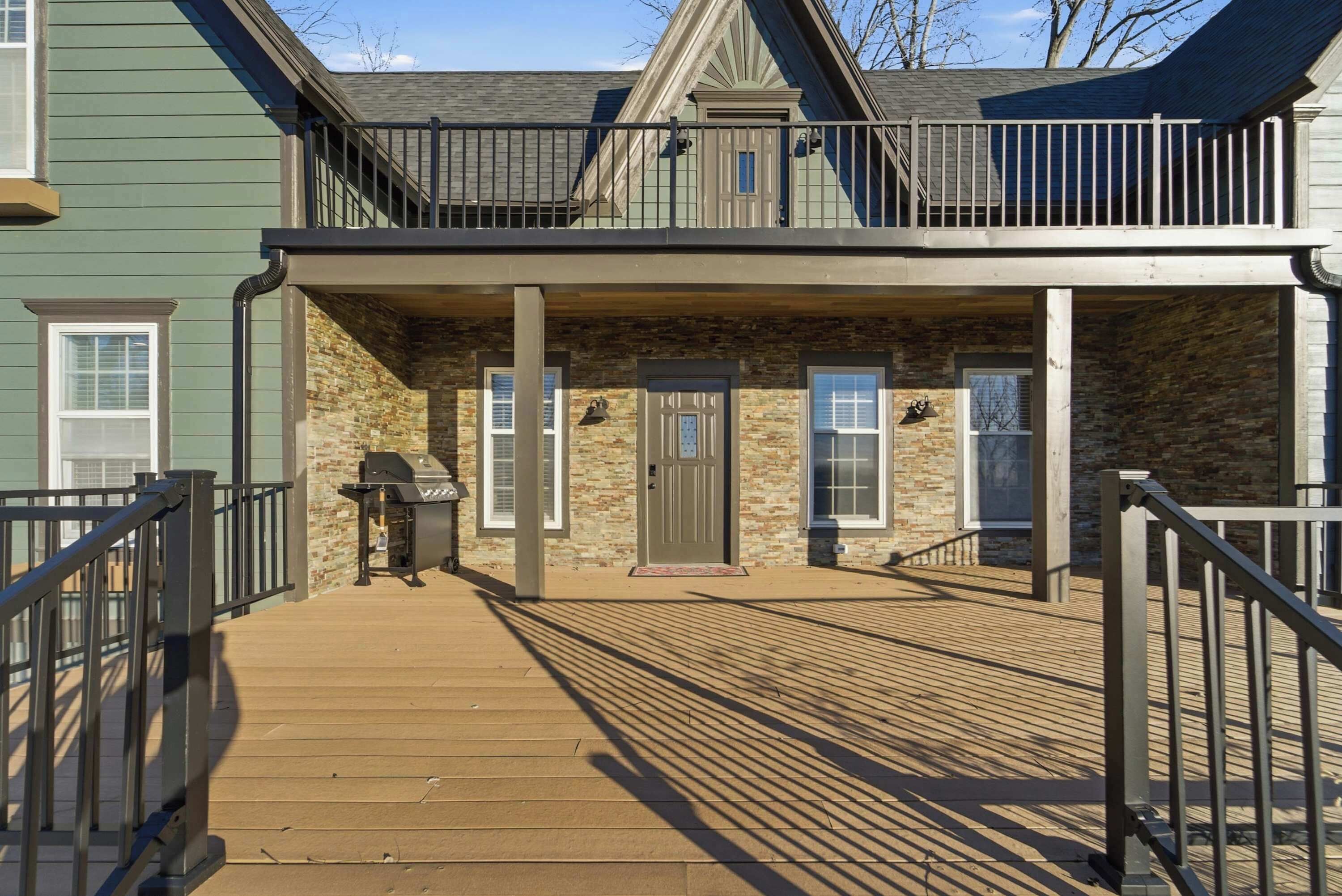 A two-story building with a covered porch, a grill, and a wooden deck.