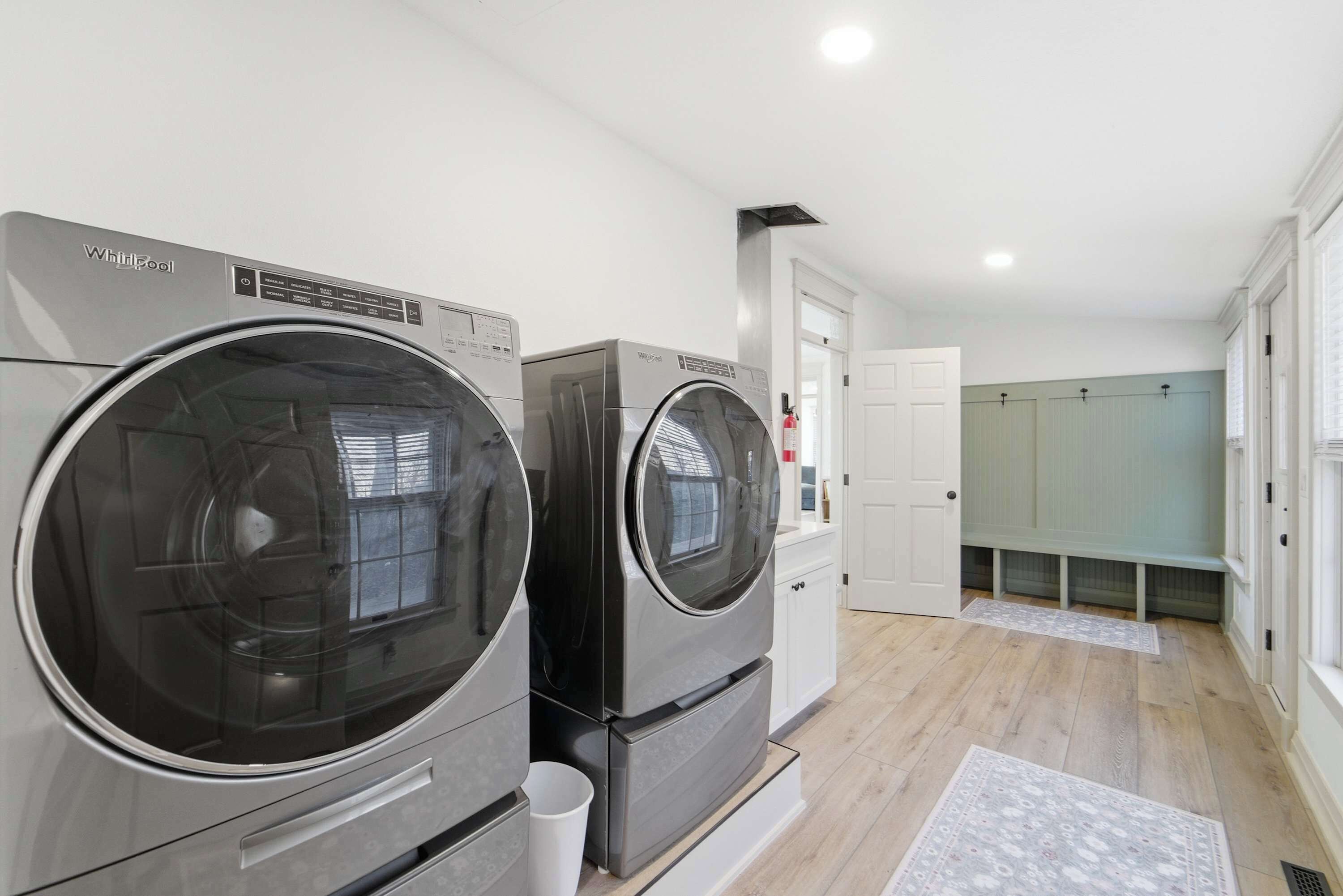 Une buanderie équipée de deux lave-linge Whirlpool, d’une porte blanche et d’un banc.