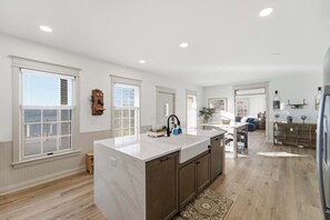 Une cuisine spacieuse dotée d’un grand îlot central, de meubles en bois et donnant sur l’espace de vie.