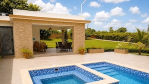 A swimming pool with a tiled edge, surrounded by a patio area with chairs and a table, and a covered seating area. - Villa la Santa, Higüey - La Altagracia (Higüey)