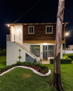 A modern two-story house with a staircase leading to the upper floor, a well-lit entrance, and a landscaped garden.